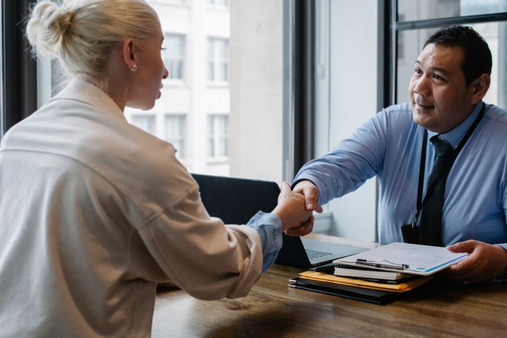 Two people shaking hands. Man is holding a paper on a clipboard in the other hand