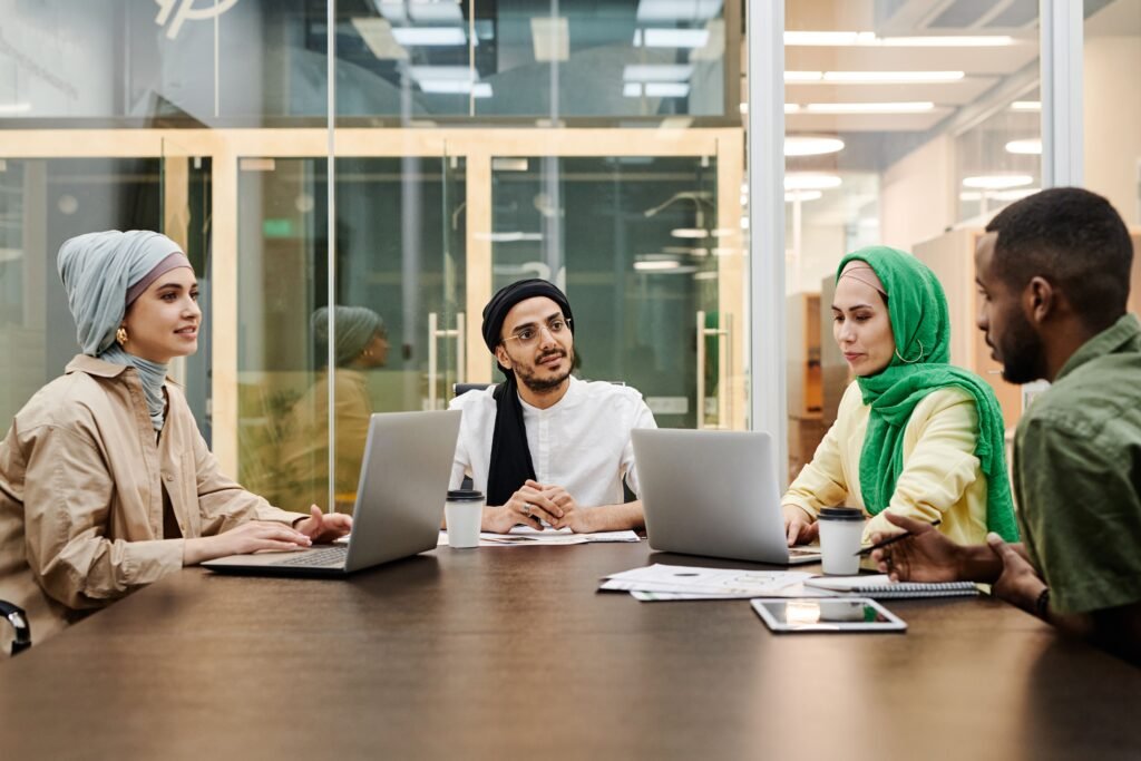 Four people sitting on the table. Two woman are sitting with laptops. Two men are discussing something important
